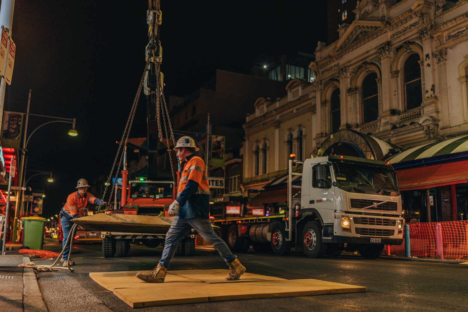 A rigger in high-vis standing on a truck bed beside a steel cage, the crane boom overhead.
