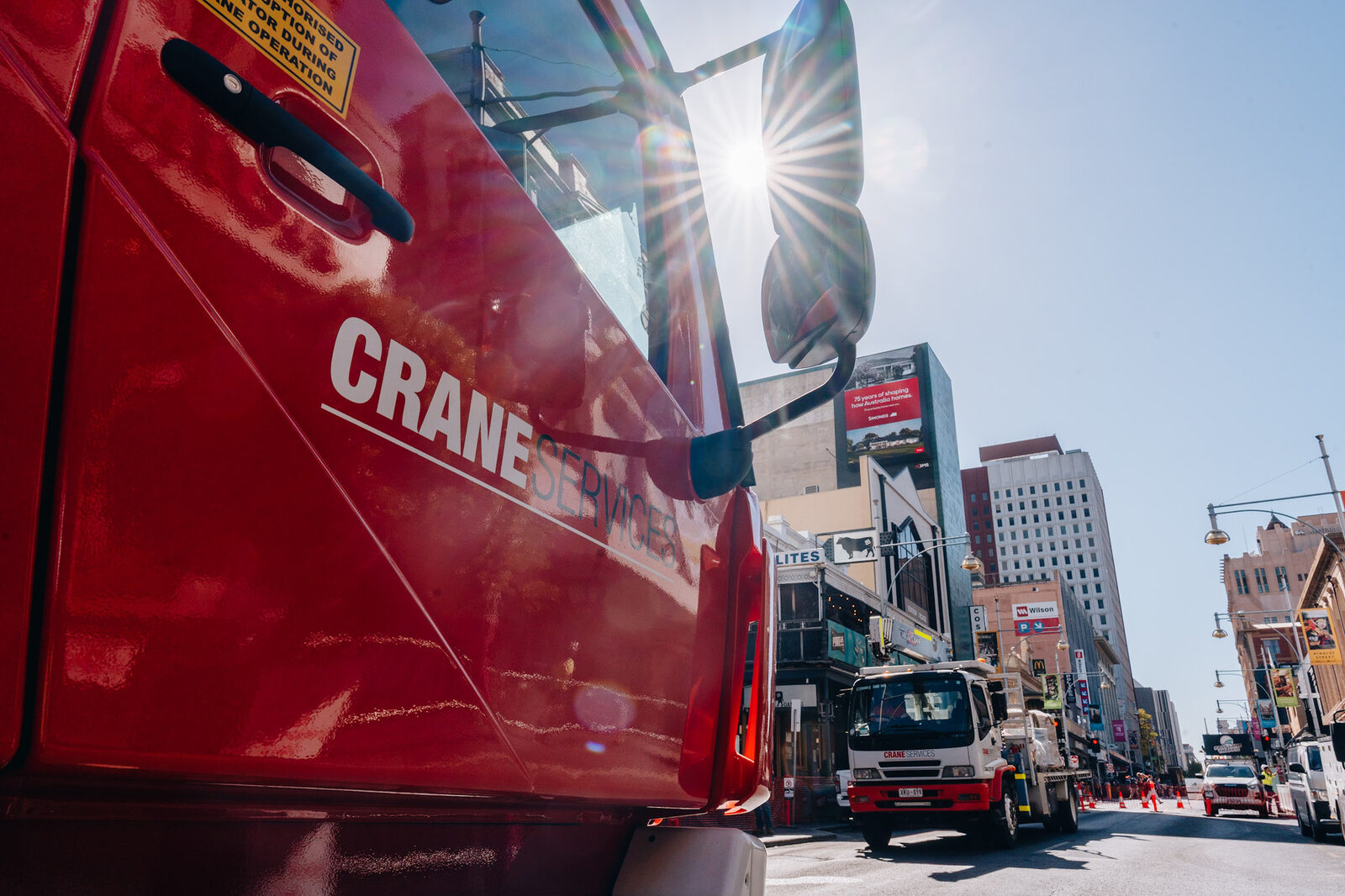 A closed city street with a crane boom arcing across the sky above the shopfronts and traffic cones.