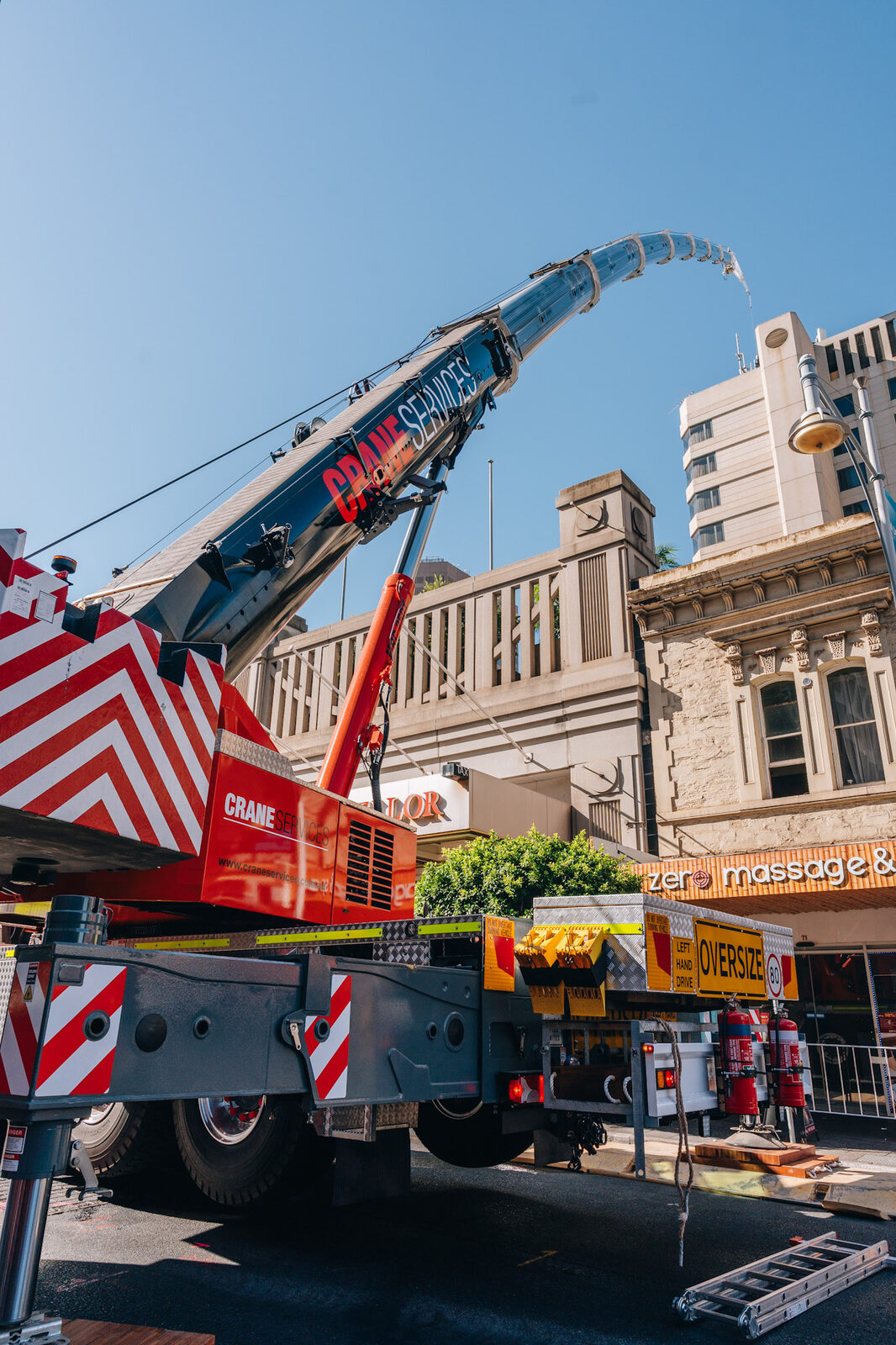A narrow laneway opening onto a street where a mobile crane stands with its boom raised.