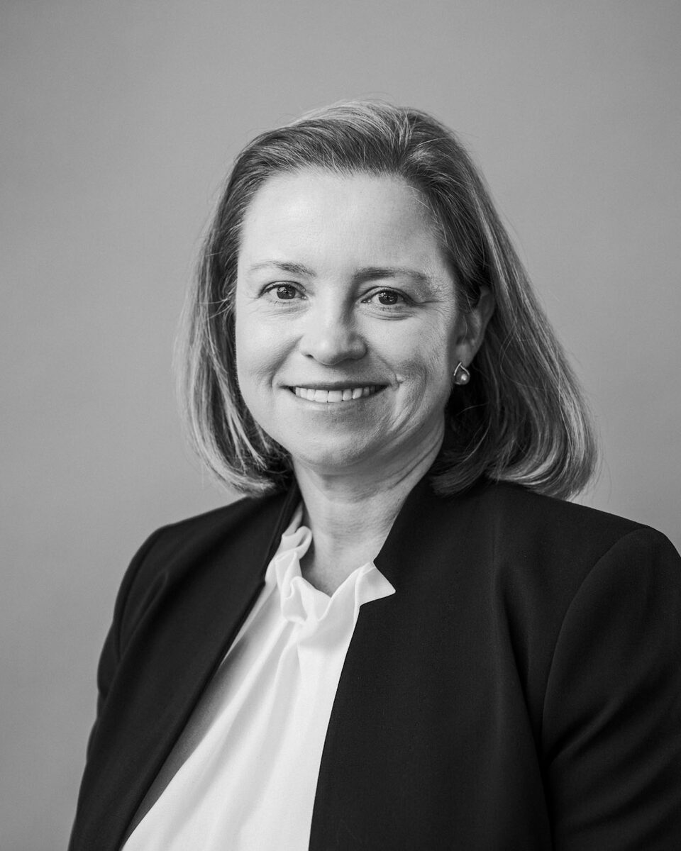 Studio headshot of a staff member in a dark blazer and white shirt against a grey backdrop.