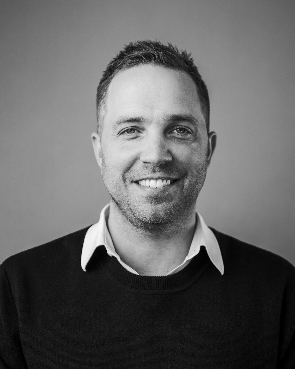Studio headshot of a smiling staff member in a navy jacket against a grey backdrop.
