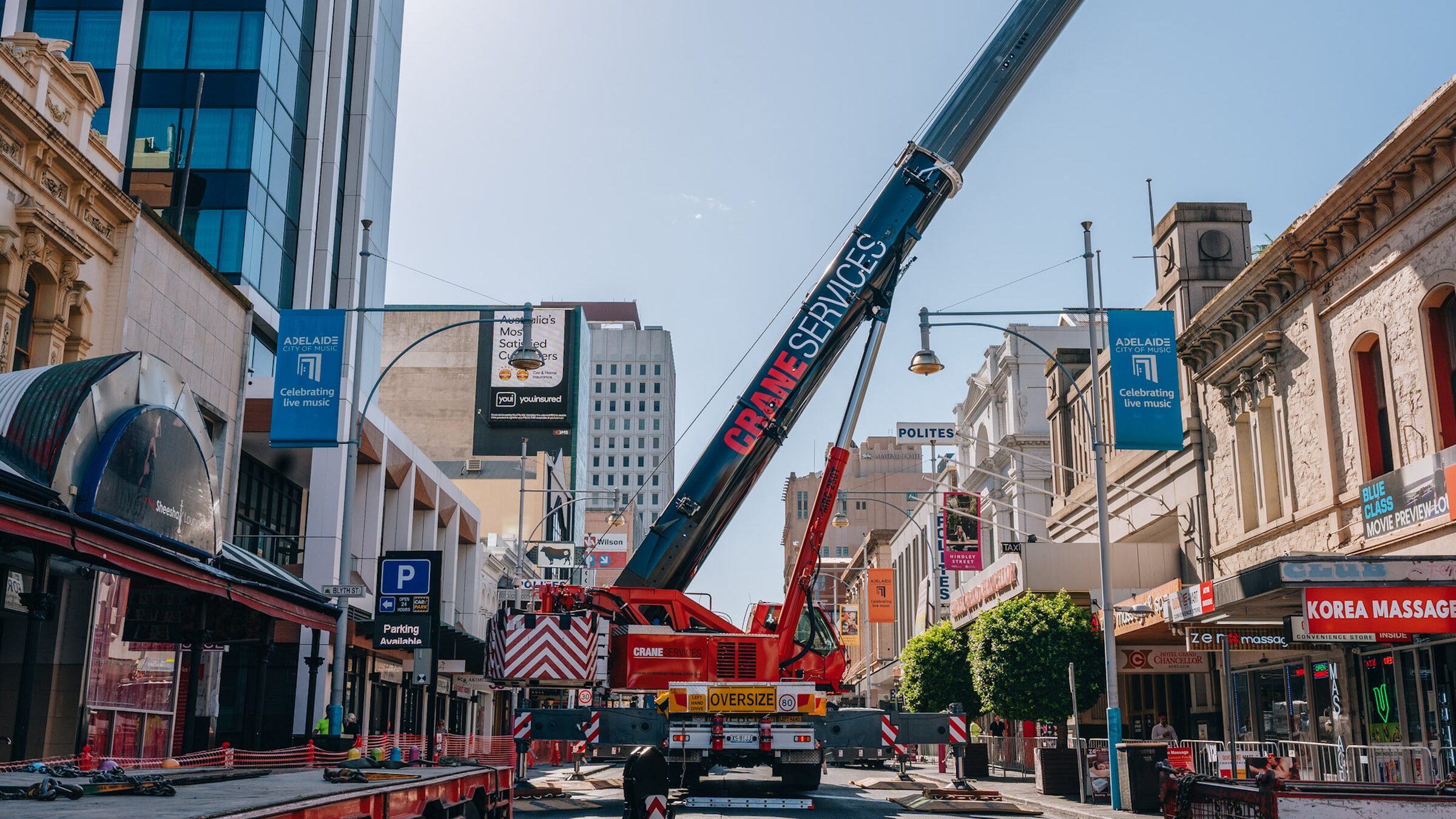 A mobile crane parked in a city street, its boom raised across the sky above heritage shopfronts.